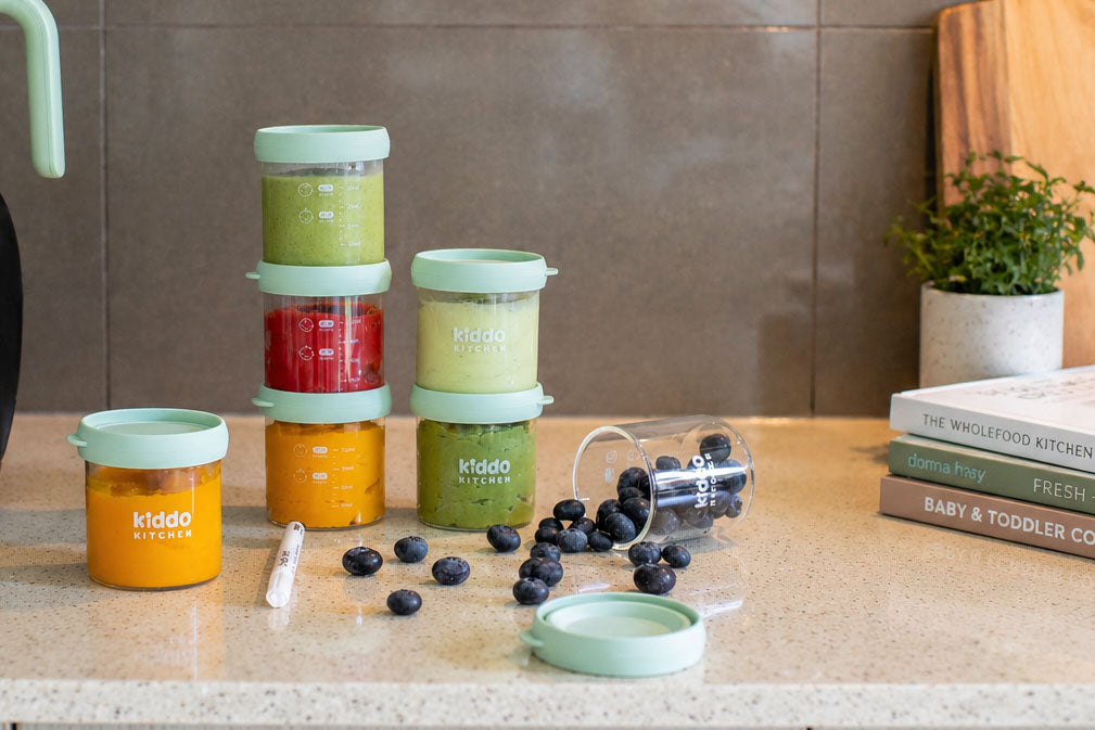 Kiddo Kitchen baby food jars filled with colourful homemade purees on a kitchen bench, with blueberries.