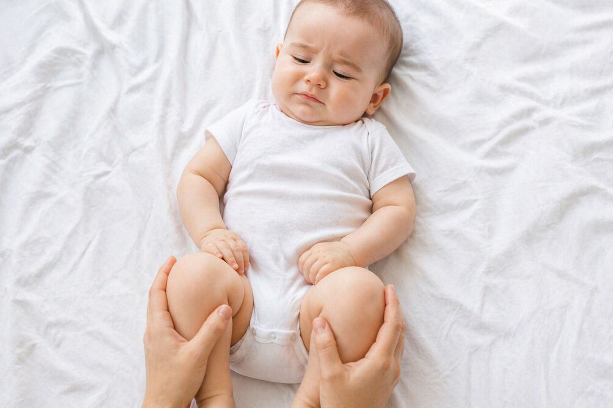 Baby with tummy discomfort after starting solids lying on back while parent supports legs